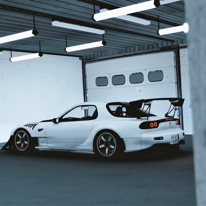 A sleek white Mazda RX-7 sports car parked in a garage under bright fluorescent lights.